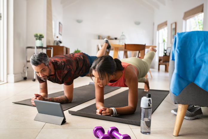 Couple faisant des exercices de renforcement musculaire à la maison guidé par une tablette