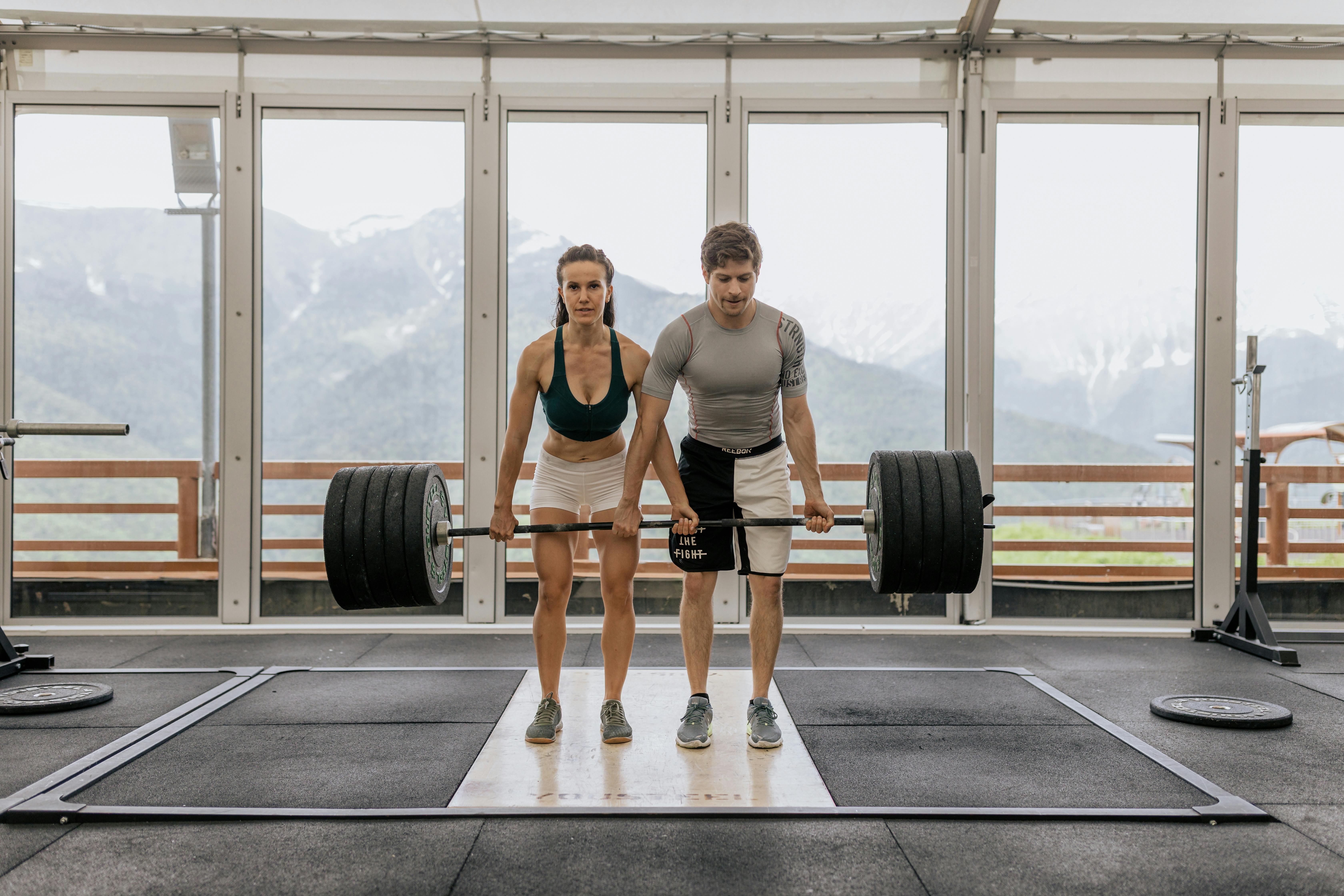 Homme et femme réalisant un exercice de musculation dans une salle avec poids libres
