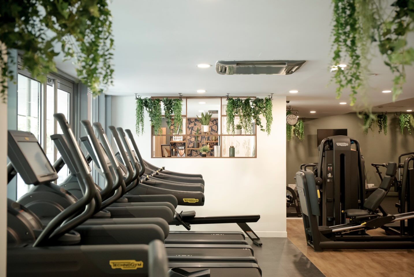 Salle de sport Leaf Circle avec rangée de tapis de course Technogym, décoration végétale suspendue et ambiance bien-être naturelle