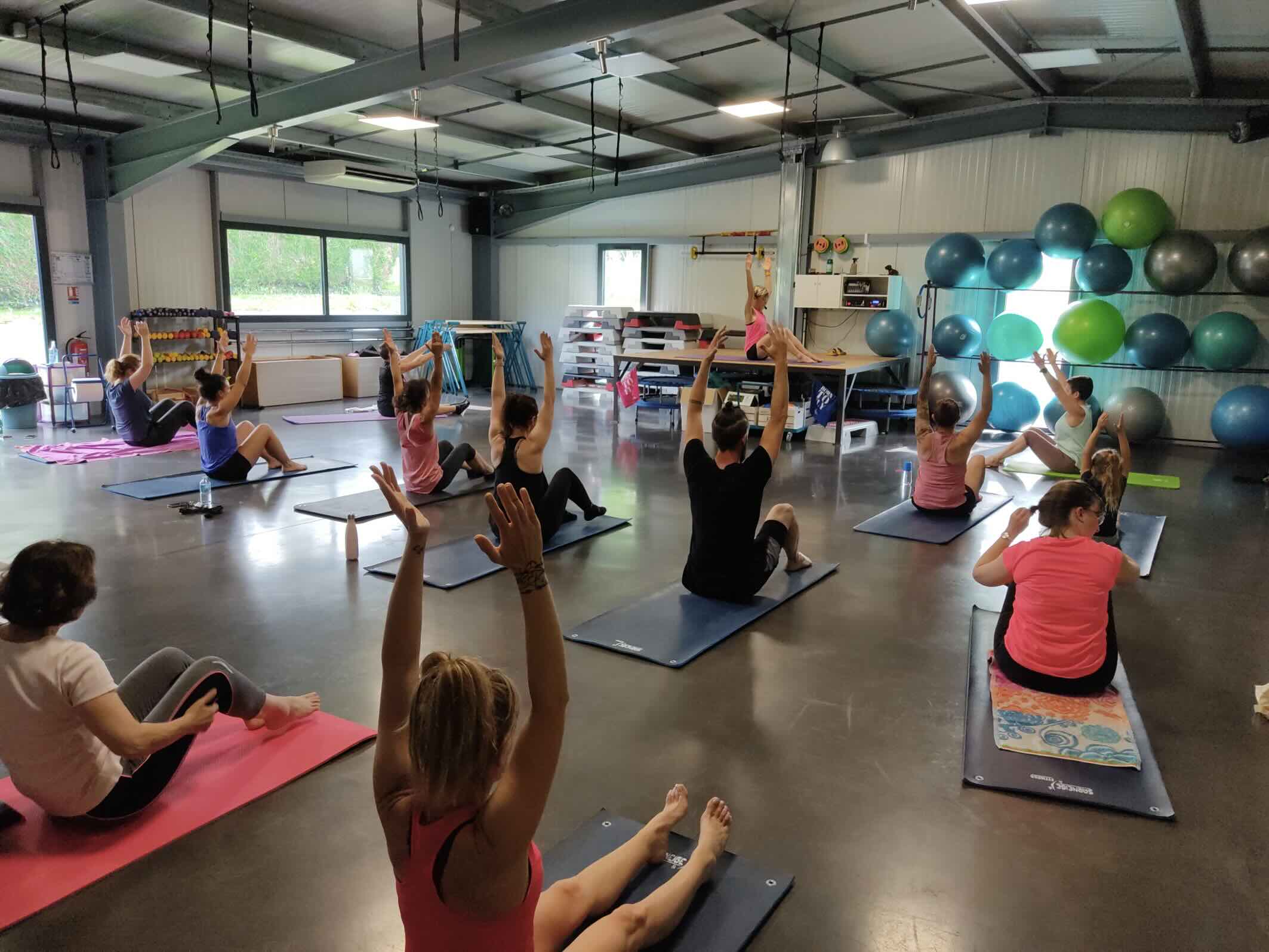 Cours collectif de gym douce chez FIT'ATTITUDE avec des participants assis sur tapis, bras levés